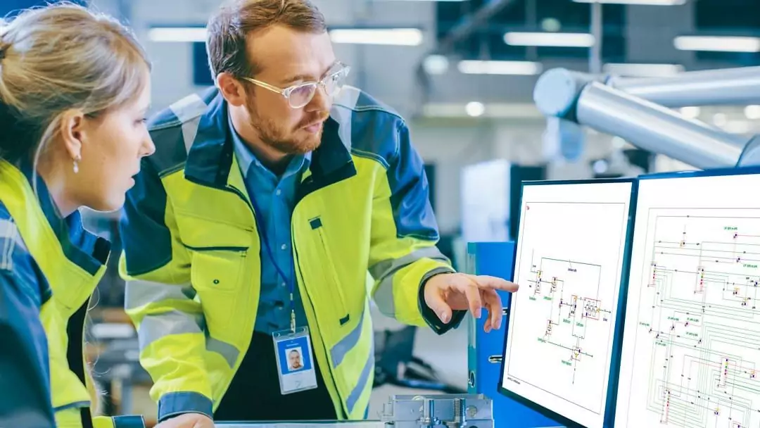 Two industrial engineers discuss a technical schematic in a manufacturing facility.